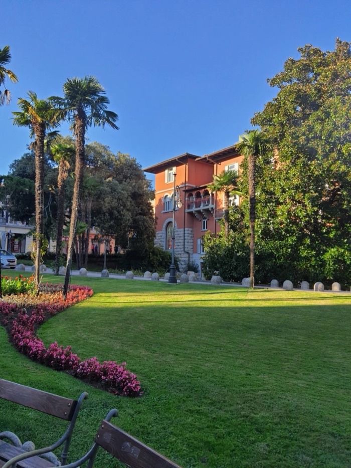 Parkanlage mit Palmen, Blumenbeet und einer historischen Villa